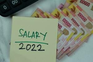 Salary 2022 write on sticky notes and Indonesian Currency isolated on Wooden Table. photo