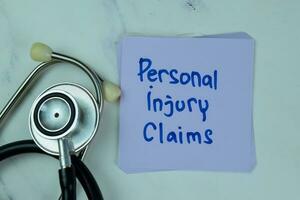 Concept of Personal Injury Claims write on sticky notes isolated on Wooden Table. photo