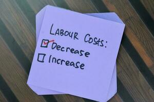 Concept of Labour Costs. Decrease or Increase write on sticky notes isolated on Wooden Table. photo