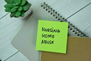 Concept of Nursing Home Abuse write on sticky notes isolated on Wooden Table. photo