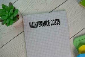 The book of Maintenance Costs isolated on Wooden Table. photo