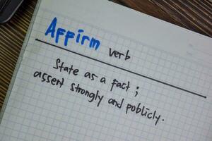 Affirm verb write on a book isolated on Wooden Table. photo