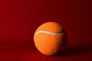 Orange tennis ball on a red background photo