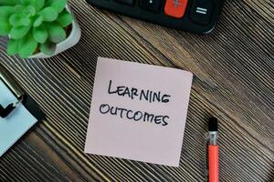 Concept of Learning Outcomes write on sticky notes isolated on Wooden Table. photo