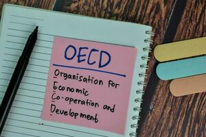 OECD - Organisation for Economic Co-operation and Development write on sticky notes isolated on Wooden Table. photo