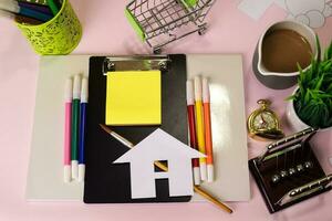 Top view of the cutting paper or drawing house on a pink table, preparing to do homework in a clipboard. Drawing Working Desk Concept photo