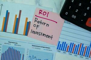 Concept of ROI - Return Of Investment write on sticky notes isolated on Wooden Table. photo