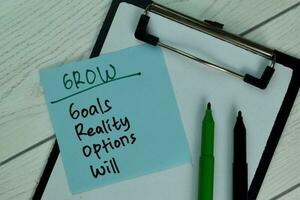 GROW - Goals Reality Options Will write on sticky note isolated on Wooden Table. photo