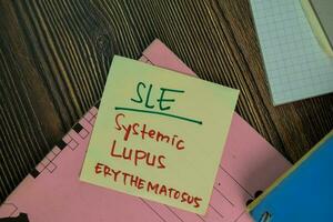 SLE - Systemic Lupus Erythematosus write on sticky notes isolated on Wooden Table. photo