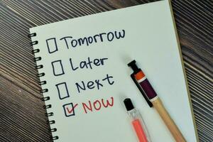 Concept of marking checkbox of now, later, next and tomorrow write on a book isolated on Wooden Table. photo