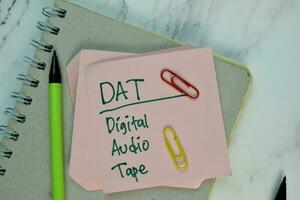 DAT - Digital Audio Tape write on sticky note isolated on Wooden Table. photo
