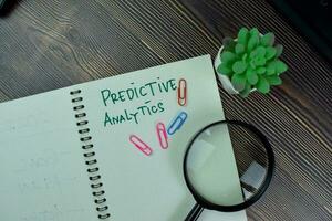 Predictive Analytics write on a book isolated on Wooden Table. photo