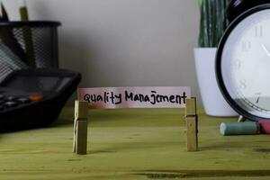 Quality Manajement. Handwriting on sticky notes in clothes pegs on wooden office desk photo