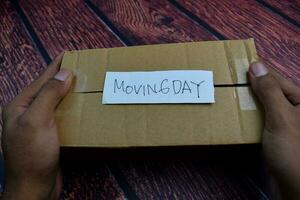 Moving Day write on a sticky note above brown box Isolated on wooden table background photo