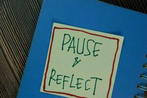 Pause and Reflect write on sticky notes isolated on Wooden Table. photo