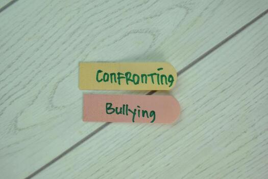 Confronting Bullying write on sticky notes isolated on Wooden Table. photo