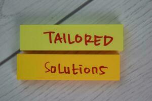 Tailored Solutions write on sticky notes isolated on Wooden Table. photo