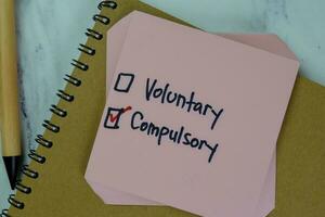 Concept of Voluntary or Compulsory write on sticky notes isolated on Wooden Table. photo
