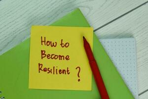 How To Become Resilient write on a book isolated on Wooden Table. photo