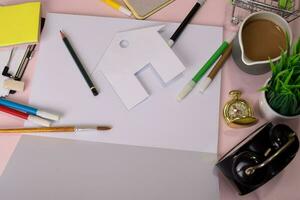 Top view of the cutting paper or drawing house on a pink table, preparing to do homework in an open notebook. Drawing Working Desk Concept. photo