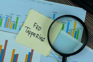 Fed Tappering write on sticky notes isolated on Wooden Table. photo