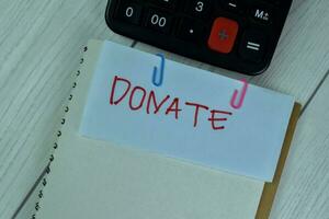 Concept of Donate write on sticky notes isolated on Wooden Table. photo