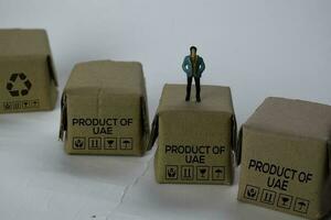 Miniature businessman Standing on Boxes with text Made in Product Of UAE isolated white bakground photo
