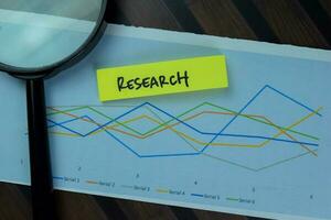 Magnifying glass and Research write on sticky notes isolated on Wooden Table. photo