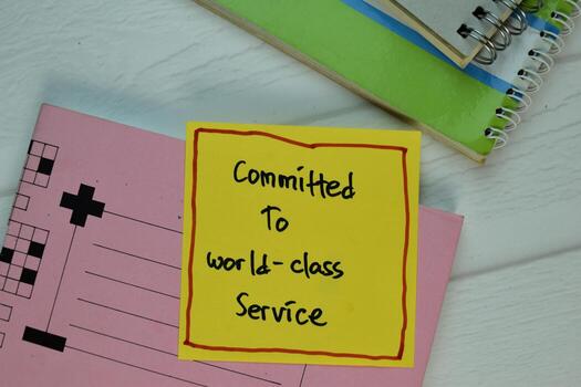 Commited to World-Class Service write on sticky note isolated on Wooden Table. photo