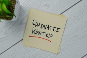 Graduates Wanted write on sticky notes isolated on Wooden Table. photo