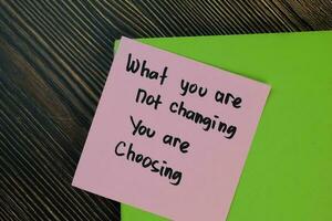 What you are not changing you are choosing write on sticky notes isolated on Wooden Table. Motivation concept photo