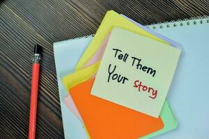 Concept of Tell Them Your Story write on sticky notes isolated on Wooden Table. photo