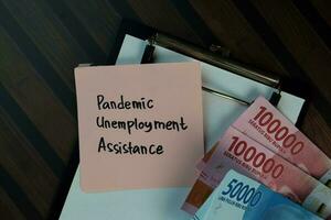 Pandemic Unemployment Assitance write on sticky notes isolated on Wooden Table. Business or Finance concept photo