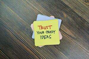 Concept of Trust Your Crazy Ideas write on sticky notes isolated on Wooden Table. photo