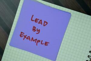 Concept of Lead by Example write on sticky notes isolated on Wooden Table. photo