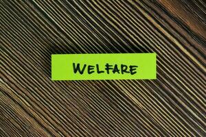 Welfare write on sticky notes isolated on Wooden Table. photo