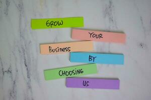 Grow Your Business By Chossing Us write on sticky notes isolated on Wooden Table. photo