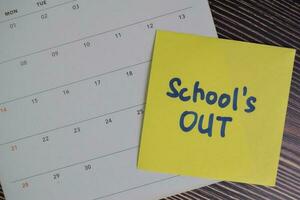 School's Out write on sticky notes and Calendar isolated on Wooden Table. photo