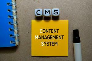 CMS - Content Management System write on Sticky note. Isolated on wooden table photo