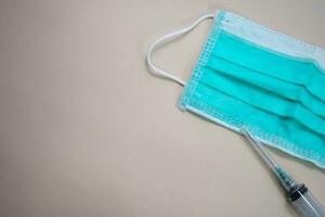 Close up protective face green mask and syringe isolated on brown background photo