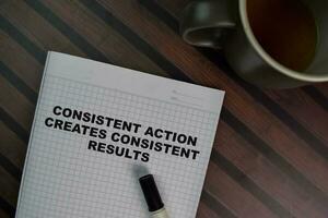 Consistent Action Creates Consistent Results write on a book isolated on Wooden Table. photo