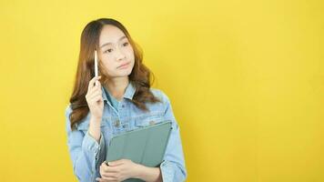 Young beautiful asian woman thinking behind yellow background video