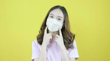 Young Asian woman in mask showing thumbs up wearing university official uniform introducing company standing on yellow background video