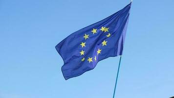 flagga av de europeisk union vinka i de vind på flaggstång mot de blå himmel. närbild av enda europeisk flagga med tolv gul stjärnor anordnad i en cirkel. video