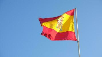 spanska nationell flagga vinka på blå himmel bakgrund. de flagga på en flaggstång fladdrar i de vind. röd med gul Spanien flagga blåser i de vind mot på blå himmel video