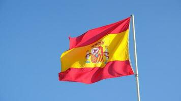 Spanish national flag waving on blue sky background. The flag on a flagpole flutters in the wind. Red with yellow Spain Flag blowing in the wind against on blue sky video