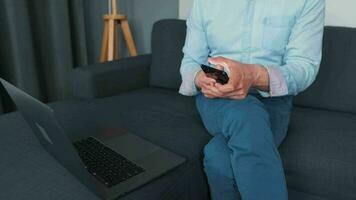 Mens zittend Aan een knus sofa en werken Aan laptop en smartphone. concept van afgelegen werk video