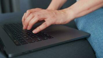 Woman sitting on a cozy sofa and working on a laptop. Concept of remote work. Close-up video