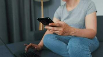 Woman sitting on a cozy sofa and working on a laptop and smartphone. Concept of remote work. Home Office video