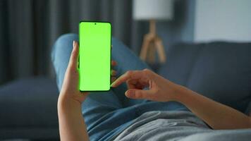 Woman at home lying on a couch and using smartphone with green mock-up screen in horizontal landscape mode. Girl browsing Internet, watching content, videos, blogs. POV. video